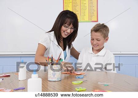 USA, Illinois, Metamora, Teacher assisting school boy (8-9) in classroom View Large Photo Image Stock Photo - USA, Illinois, Metamora, Teacher assisting school boy (8-9) in classroom. Fotosearch