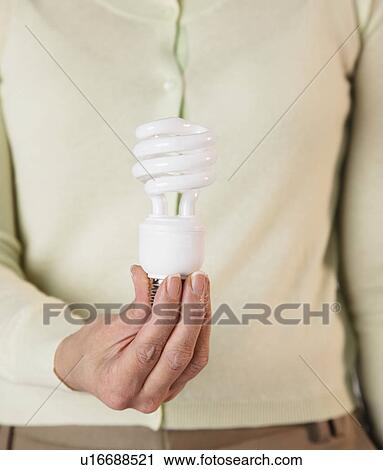 Stock Image - USA, Illinois, Metamora, Woman holding energy saving lightbulb, mid section. Fotosearch
