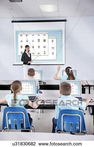 Stock Image - USA, Illinois, Metamora, Woman teaching children (8-9, 10-11) in computer lab. Fotosearch