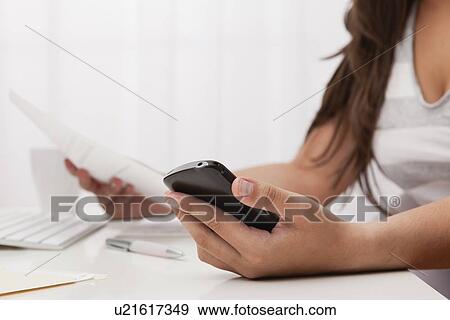 Stock Photo - USA, Illinois, Metamora, Woman texting on his mobile in office. Fotosearch