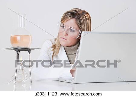 Stock Image - USA, Illinois, Metamora, woman working with laptop and laboratory glassware. Fotosearch