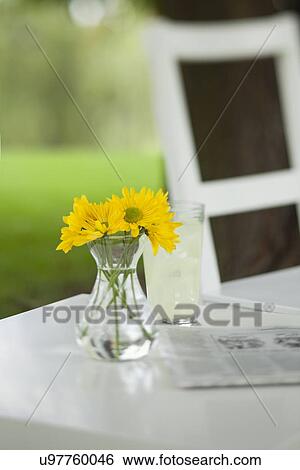Stock Photograph - USA, Illinois, Metamora, Yellow flowers in vase and newspaper on table. Fotosearch