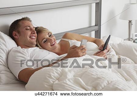 Picture - USA, Illinois, Metamora, Young couple text-messaging in bed. Fotosearch