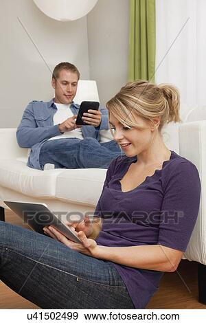 USA, Illinois, Metamora, Young couple with e-books relaxing in living room View Large Photo Image Stock Photo - USA, Illinois, Metamora, Young couple with e-books relaxing in living room. Fotosearch