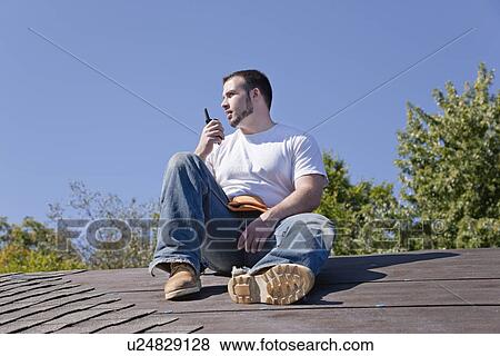 Stock Photo - USA, Illinois, Metamora, Young man sitting on roof and talking via walki talkie. Fotosearch