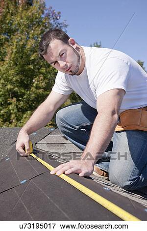 Stock Photo - USA, Illinois, Metamora, Young man measuring roof. Fotosearch
