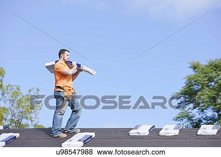 Stock Photo - USA, Illinois, Metamora, Young man working on roof. Fotosearch
