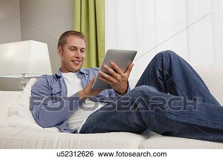 USA, Illinois, Metamora, Young man using tablet pc in living room View Large Photo Image Stock Photograph - USA, Illinois, Metamora, Young man using tablet pc in living room. Fotosearch