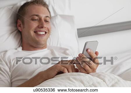 USA, Illinois, Metamora, Young man text-messaging in bed View Large Photo Image Stock Photograph - USA, Illinois, Metamora, Young man text-messaging in bed. Fotosearch