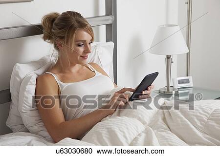 Stock Image - USA, Illinois, Metamora, Young woman reading e-book in bed. Fotosearch