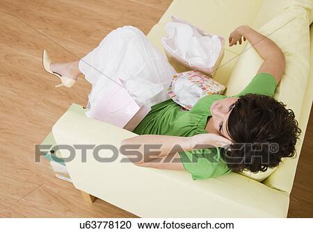 Stock Image - USA, Illinois, Metamora, Young woman with shopping bags sitting on sofa in shoes store and laughing. Fotosearch