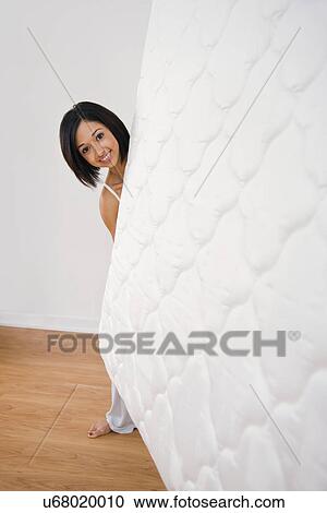 Stock Image - USA, Illinois, Metamora, Young woman holding mattress and looking at camera. Fotosearch