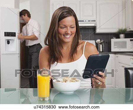 Stock Image - USA, Illinois, Metamora, young woman having breakfast cereal and holding digital tablet. Fotosearch