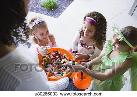 Stock Image - USA, Illinois, Metamora, Young woman giving candies to girls (6-7, 8-9) in costumes during Halloween. Fotosearch