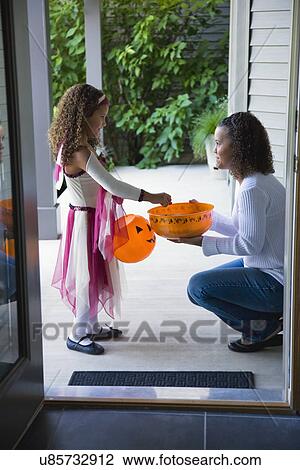 Stock Image - USA, Illinois, Metamora, Young woman giving candies to girl (6-7) in costume during Halloween. Fotosearch