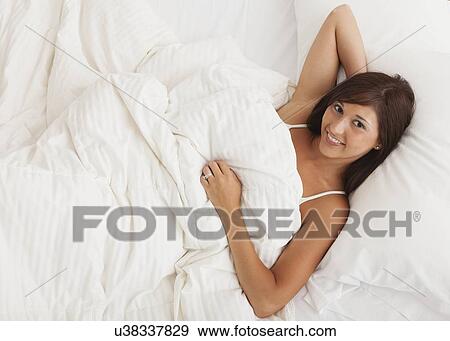Stock Photo - USA, Illinois, Metamora, young woman lying down in bed. Fotosearch
