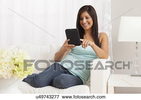Stock Photo - USA, Illinois, Metamora, Young woman with digital table sitting on sofa. Fotosearch