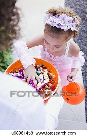 Stock Photo - USA, Illinois, Metamora, Young woman giving candies to girl (6-7) in costume during Halloween. Fotosearch