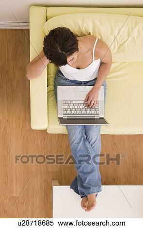 Stock Photography - USA, Illinois, Metamora, Young woman sitting on sofa with laptop. Fotosearch