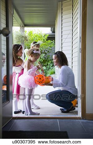 Stock Photography - USA, Illinois, Metamora, Young woman giving candies to girls (6-7, 8-9) in costumes during Halloween. Fotosearch
