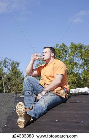 Stock Image - USA, Illinois, Metamora, Young worker sitting on roof and drinking water. Fotosearch