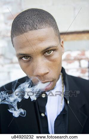 Stock Image - USA, Illinois, Peoria, Portrait of young man smoking. Fotosearch