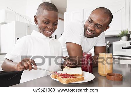 Stock Image - USA, Metamora, Illinois, Boy (6-7) with father preparing jam sandwich. Fotosearch