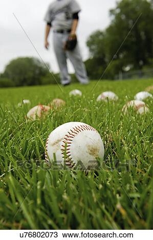 Stock Image - USA, Minnesota, Roseville, baseballs in grass, defocused man in background. Fotosearch