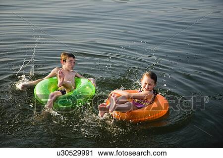 Stock Image - USA, Missouri, Stockton, Stockton Lake, boy (6-7) and girl (8-9) swimming in inflatable rings. Fotosearch