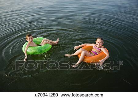 Stock Image - USA, Missouri, Stockton, Stockton Lake, boy (6-7) and girl (8-9) swimming in inflatable rings. Fotosearch
