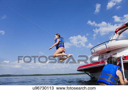 Stock Image - USA, Missouri, Stockton, Stockton Lake, girl (8-9) jumping off boat, boy (6-7) watching. Fotosearch