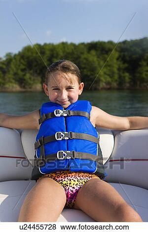 Stock Photo - USA, Missouri, Stockton, Stockton Lake, girl (8-9) wearing lifejacket sitting on boat. Fotosearch