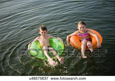 Stock Photo - USA, Missouri, Stockton, Stockton Lake, boy (6-7) and girl (8-9) swimming in inflatable rings. Fotosearch