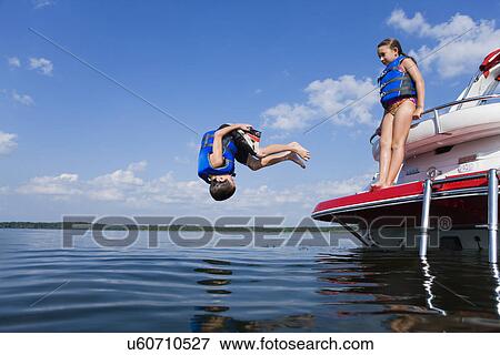 Stock Photo - USA, Missouri, Stockton, Stockton Lake, boy (6-7) jumping off boat, girl (8-9) watching. Fotosearch