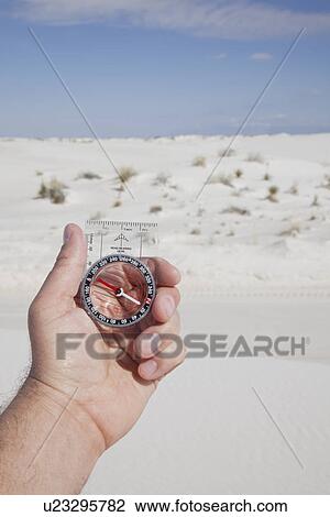 Stock Image - USA, New Mexico, Whitesands, Hand holding compass on desert. Fotosearch