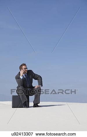 Stock Photo - USA, New Mexico, Whitesands, Man wearing suit sitting on desert. Fotosearch