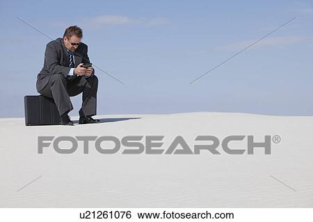 Stock Photograph - USA, New Mexico, Whitesands, Man wearing suit sitting on desert. Fotosearch