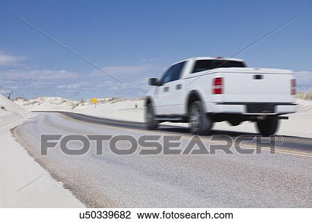 Stock Image - USA, New Mexico, Whitesands, Pick-up truck driving desert road. Fotosearch