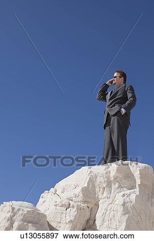 Stock Photo - USA, New Mexico, Whitesands, Businessman at the edge of rock talking via phone. Fotosearch