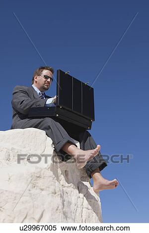 USA, New Mexico, Whitesands, Businessman holding briefcase while sitting at the edge of rock View Large Photo Image Stock Photography - USA, New Mexico, Whitesands, Businessman holding briefcase while sitting at the edge of rock. Fotosearch