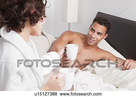 Stock Photo - USA, New York City, couple drinking morning coffee in bed. Fotosearch