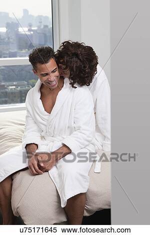 Stock Photography - USA, New York City, couple sitting on bed, woman kissing man. Fotosearch