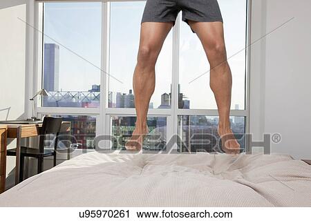 Stock Image - USA, New York City, low section of man jumping on bed. Fotosearch
