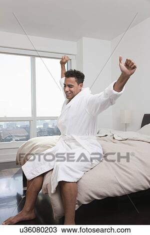 Stock Image - USA, New York City, man stretching on bed. Fotosearch
