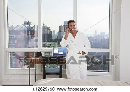 Stock Image - USA, New York City, man talking on phone in bedroom. Fotosearch