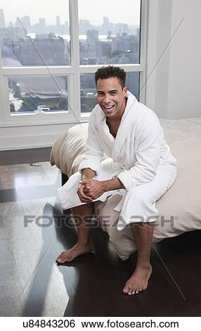 Stock Photograph - USA, New York City, portrait of man sitting on bed. Fotosearch