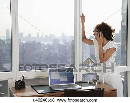 Stock Photo - USA, New York City, woman talking on phone and looking out window. Fotosearch