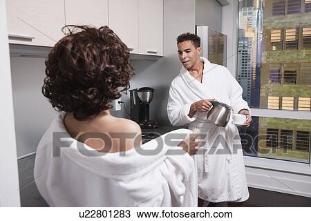 Stock Image - USA, New York City, woman undressing in front of man in kitchen. Fotosearch