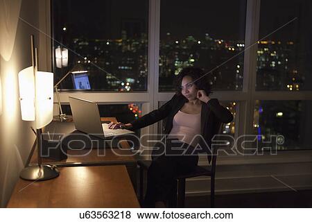 Stock Photo - USA, New York City, woman using laptop in bedroom. Fotosearch