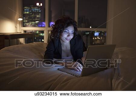 Stock Photography - USA, New York City, woman using laptop in bedroom. Fotosearch